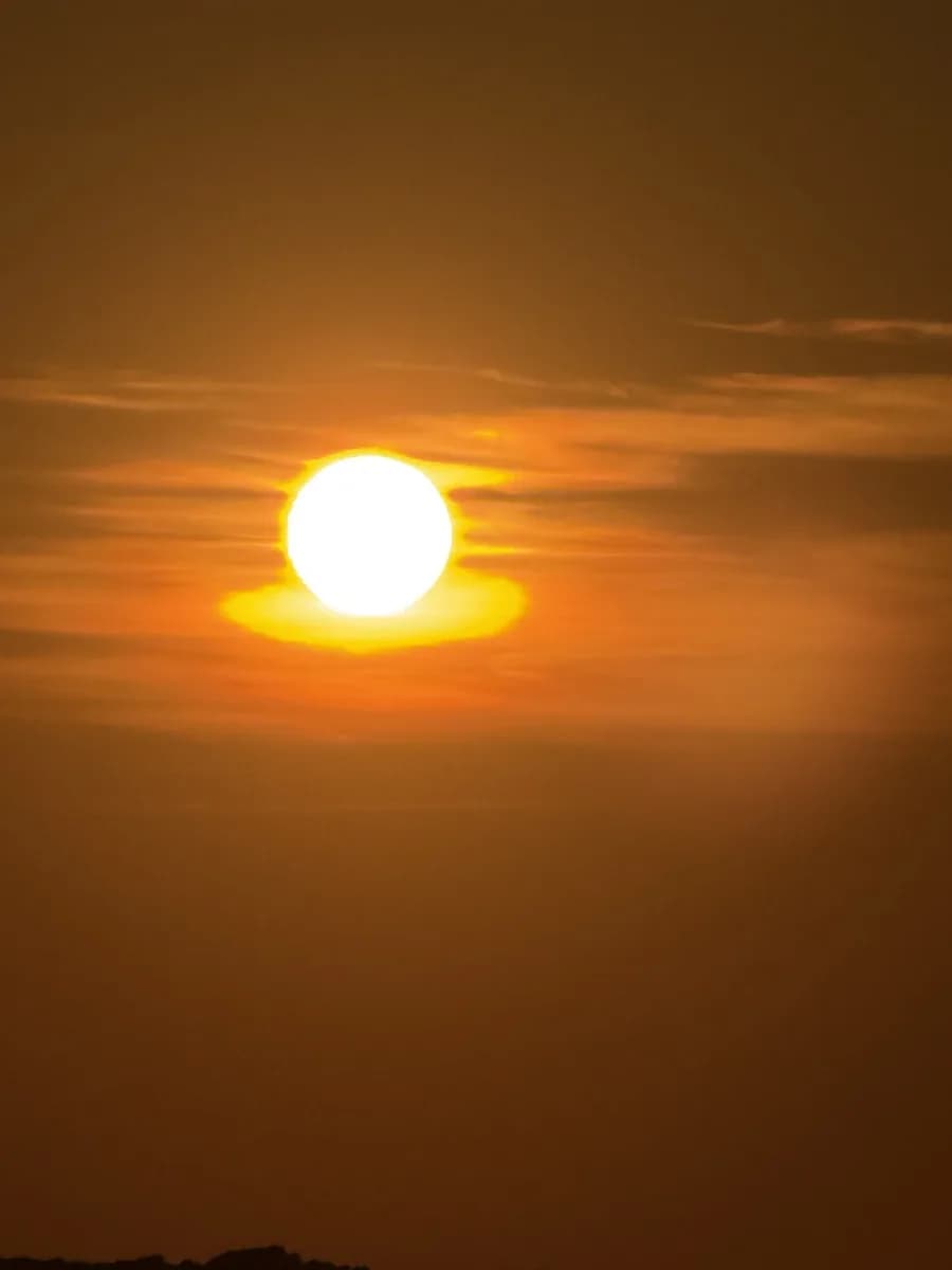 The sun close to the horizon in a haze of amber cloud over the bay